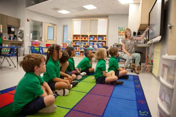Children sitting on colorful rug watching teacher present